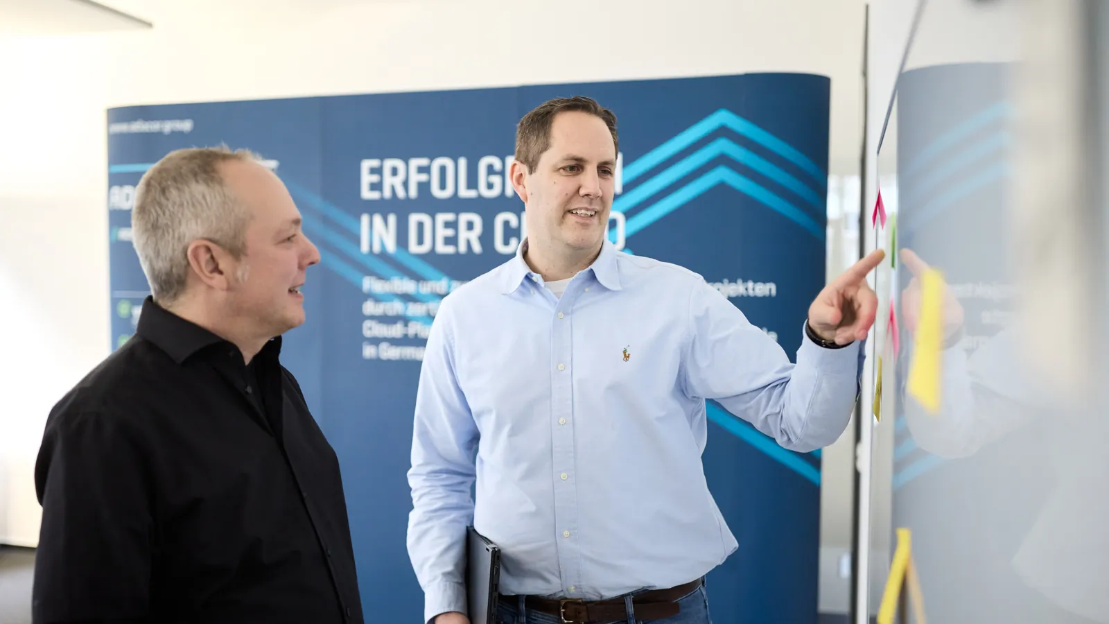 Hybrid Cloud planen: zwei Adacor-Kollegen besprechen eine Cloud-Architektur vor dem Banner „Erfolgreich in der Cloud“