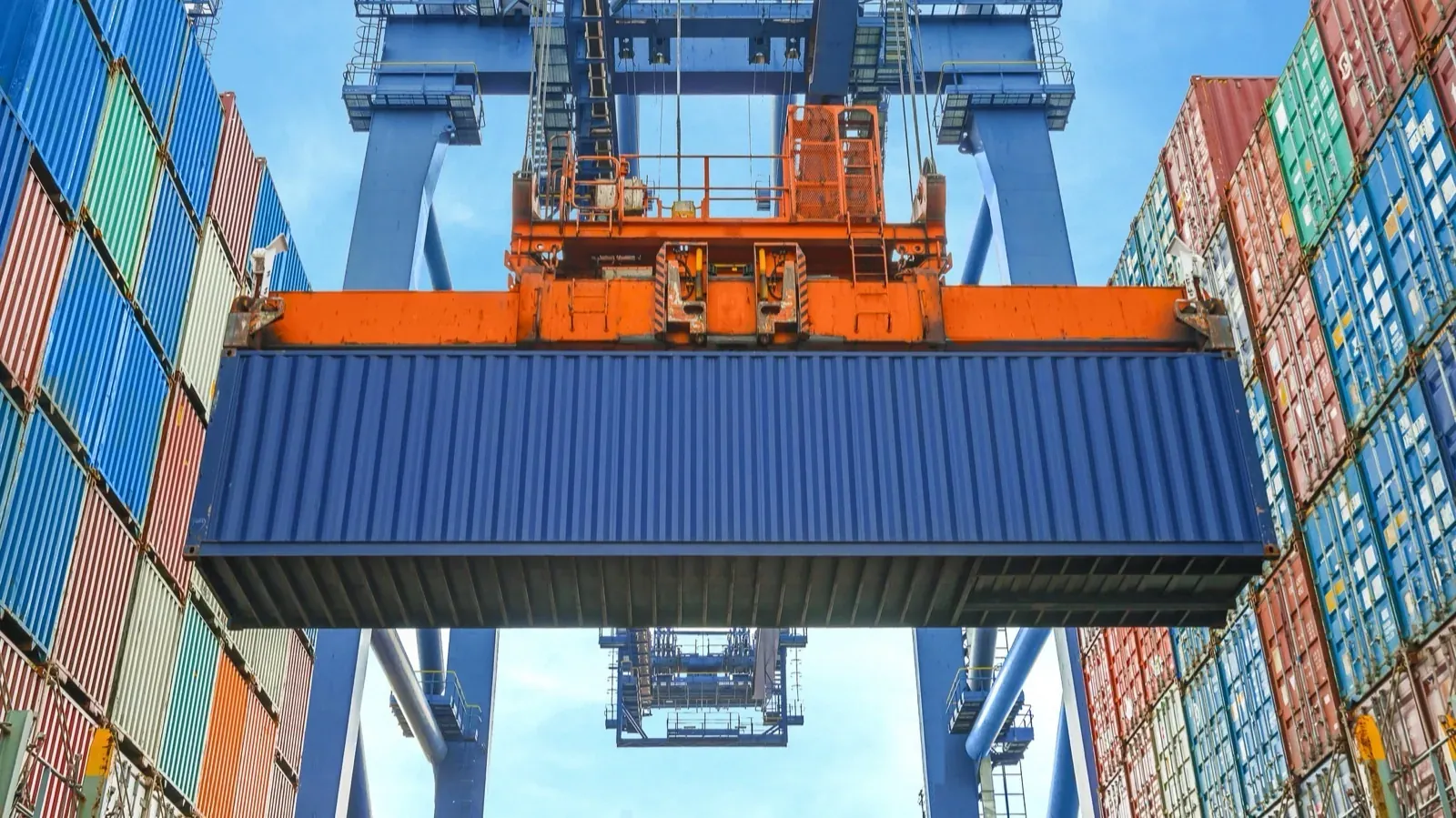 Container wird von einem Hafenkran zwischen Containerstapeln bewegt – Sinnbild für Container-Orchestrierung mit Kubernetes
