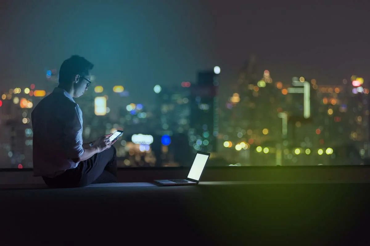 IT-Verantwortlicher wertet abends Kennzahlen aus – Laptop und Smartphone vor nächtlicher Skyline